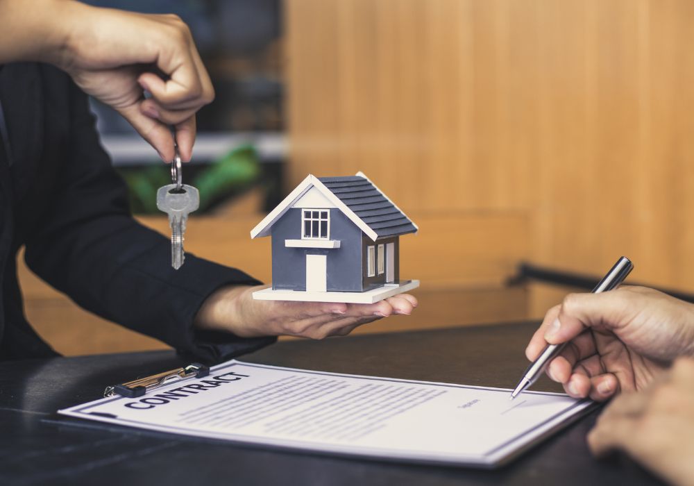 An image of someone holding a key and small house with someone signing documents